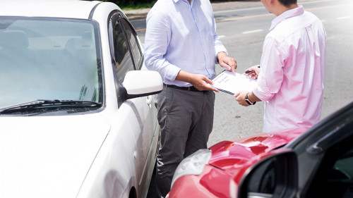 Insurance agent writing on clipboard while examining car after a
