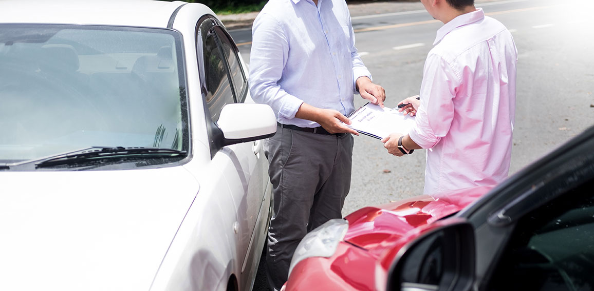 Insurance agent writing on clipboard while examining car after a