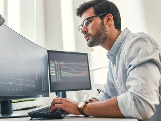 Confident businessman. Young bearded trader in formal wear is analyzing trading charts on computer screens while sitting in his modern office
