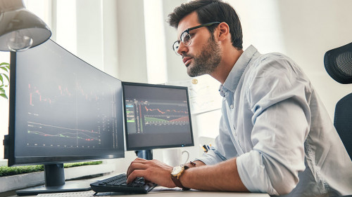 Confident businessman. Young bearded trader in formal wear is analyzing trading charts on computer screens while sitting in his modern office