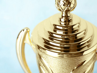 Shiny golden trophy cup on blue background, closeup