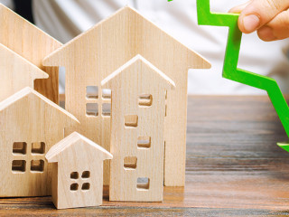 Analyst holds down arrow near the wooden houses. Concept of falling real estate market. Low prices and cost of housing. Reduced mortgage rates and housing demand. Bankruptcy. Crisis and low liquidity