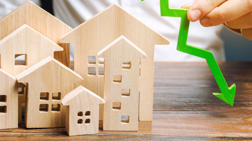 Analyst holds down arrow near the wooden houses. Concept of falling real estate market. Low prices and cost of housing. Reduced mortgage rates and housing demand. Bankruptcy. Crisis and low liquidity