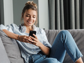 Image of smiling nice woman using cellphone while sitting on sof