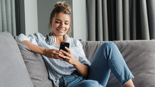 Image of smiling nice woman using cellphone while sitting on sof