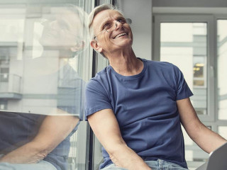 Happy elderly man sitting with gadget on knees
