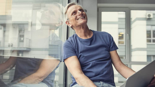 Happy elderly man sitting with gadget on knees