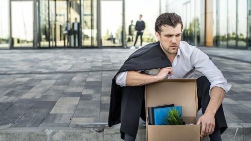 Fired businessman sitting on street