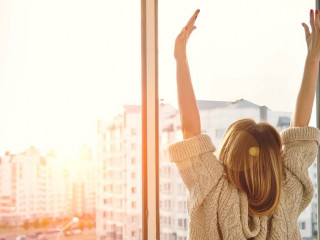 Woman near window raising hands facing the sunrise at morning