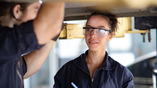 Hispanic Female trainee Mechanics Working Underneath Car Togethe