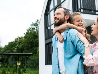 happy man piggybacking daughter near cheerful wife and house