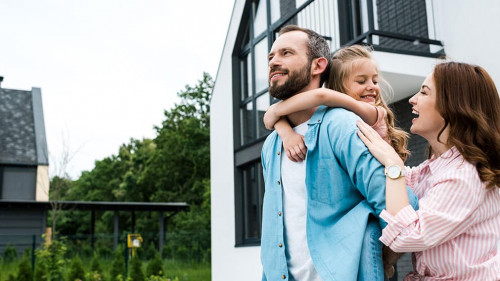 happy man piggybacking daughter near cheerful wife and house