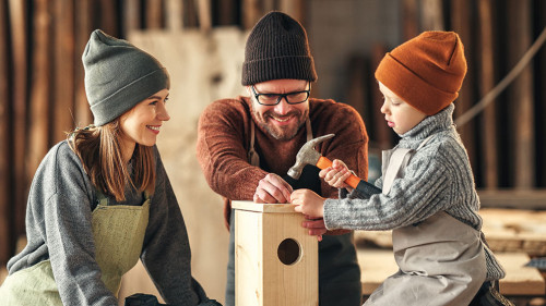 Kid with parents assembling wooden bird house in craft workshop