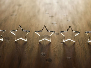 3D render: Five star rating - five transparent acrylic glas stars standing on a wooden table. Selective focus and copy space.
