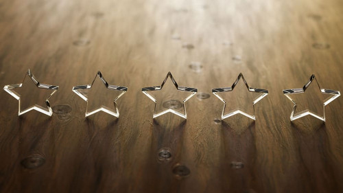 3D render: Five star rating - five transparent acrylic glas stars standing on a wooden table. Selective focus and copy space.