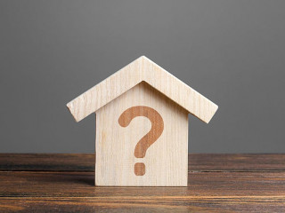 Question mark on a wooden house. Solving housing problems, deciding to buy or rent real estate. Search for options, the choice of accommodation between apartment and house. Cost estimate