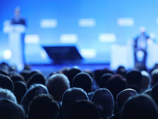 Business and entrepreneurship symposium. Speaker giving a talk at business meeting. Audience in the conference hall. Rear view of unrecognized participant in audience.