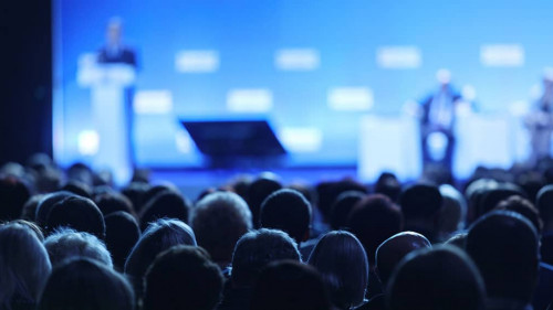 Business and entrepreneurship symposium. Speaker giving a talk at business meeting. Audience in the conference hall. Rear view of unrecognized participant in audience.