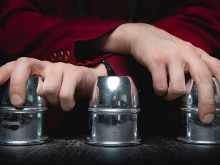 Magician shows shell game of thimbles with circles and ball, black background. Concept deception, sleight hand