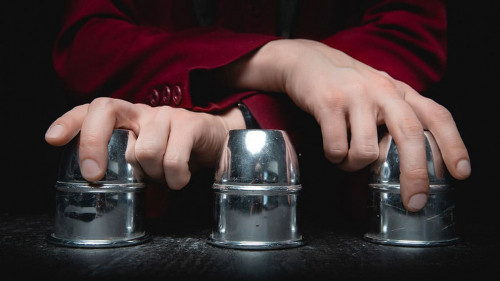 Magician shows shell game of thimbles with circles and ball, black background. Concept deception, sleight hand