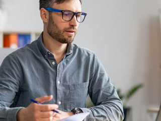 Successful middle aged businessman working at office, sitting at workdesk in front of laptop and taking notes