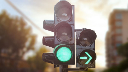 Green traffic light with green arrow light up in city while suns