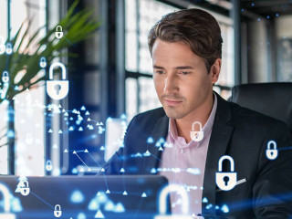 Handsome businessman in suit at workplace working with laptop to defend customer cyber security. Concept of clients information protection and brainstorm. Padlock hologram over office background.