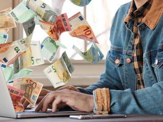 Man with modern laptop and flying euro banknotes at table indoor