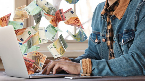 Man with modern laptop and flying euro banknotes at table indoor