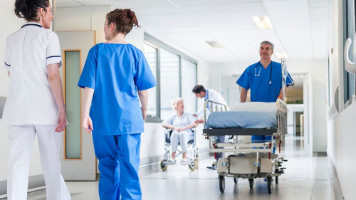 Male nurse pushing stretcher gurney bed in hospital corridor wit