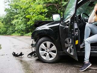 Young woman in the damaged car after a car accident, making a phone call.