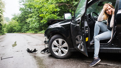 Young woman in the damaged car after a car accident, making a phone call.