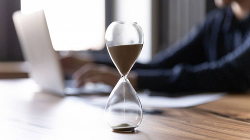 Crop of hourglass on table with employee working on background