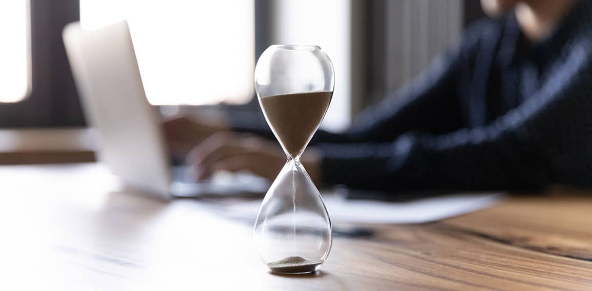 Crop of hourglass on table with employee working on background