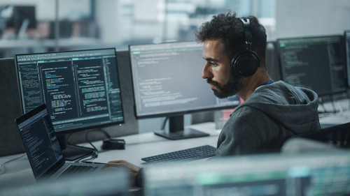 Office: Professional White IT Programmer Uses Headphones while W