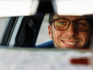 Cheerful man adjusting mirror while sitting in his car, looking