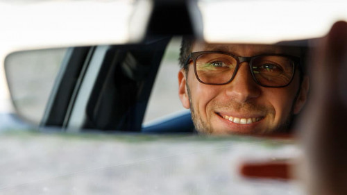 Cheerful man adjusting mirror while sitting in his car, looking