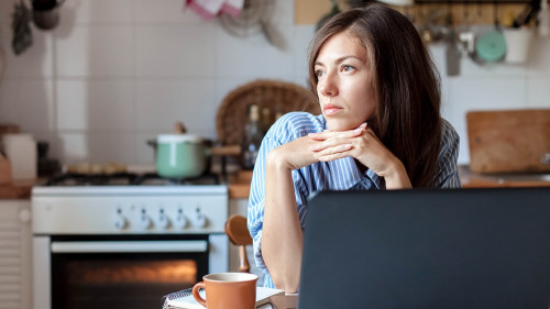Working from home office. Upset woman using laptop and Internet. Freelancer workplace at kitchen table.