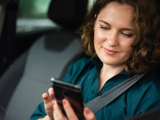 Woman driver sitting in car and looking at smartphone screen