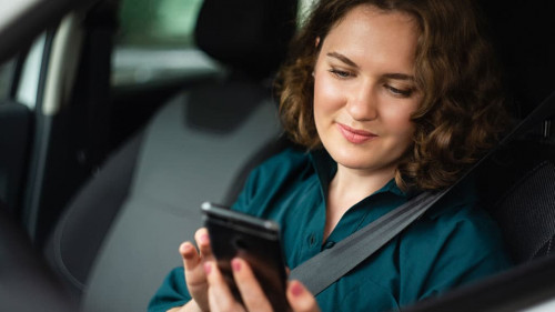 Woman driver sitting in car and looking at smartphone screen