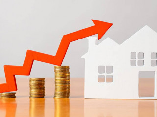 Coins on a table, a red up arrow and house. The concept of the rising price of real estate