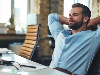 Work done. Satisfied young bearded businessman leaning back with hands behind head and relaxing while sitting in the modern office