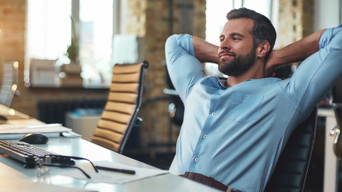 Work done. Satisfied young bearded businessman leaning back with hands behind head and relaxing while sitting in the modern office