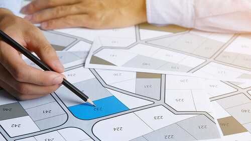 Man holding a pencil pointing to cadastral map to decide to buy