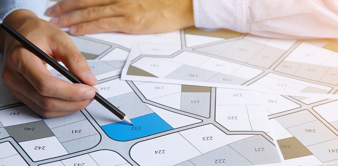 Man holding a pencil pointing to cadastral map to decide to buy