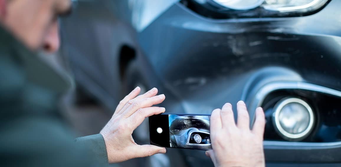 Male Driver Taking Photo Of Damaged Car After Accident For Insur