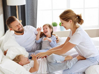 happy family mother, father and children laughing, playing and tickles in bed at home