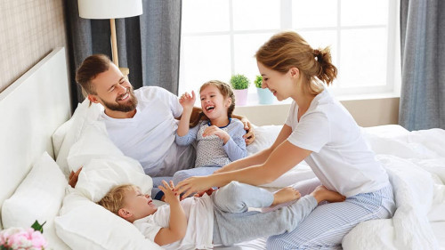 happy family mother, father and children laughing, playing and tickles in bed at home