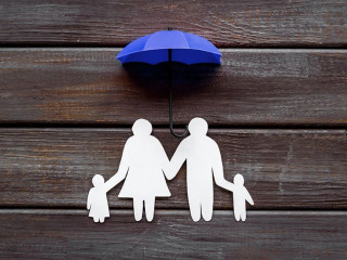 Health insurance concept. Family cutout under umbrella on dark wooden background top-down copy space