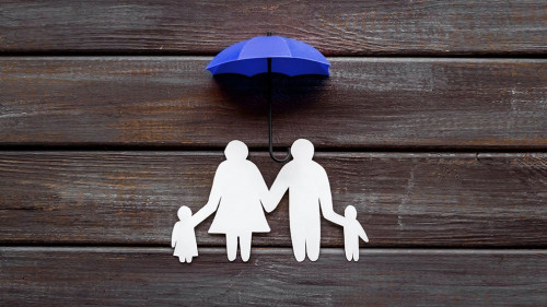 Health insurance concept. Family cutout under umbrella on dark wooden background top-down copy space